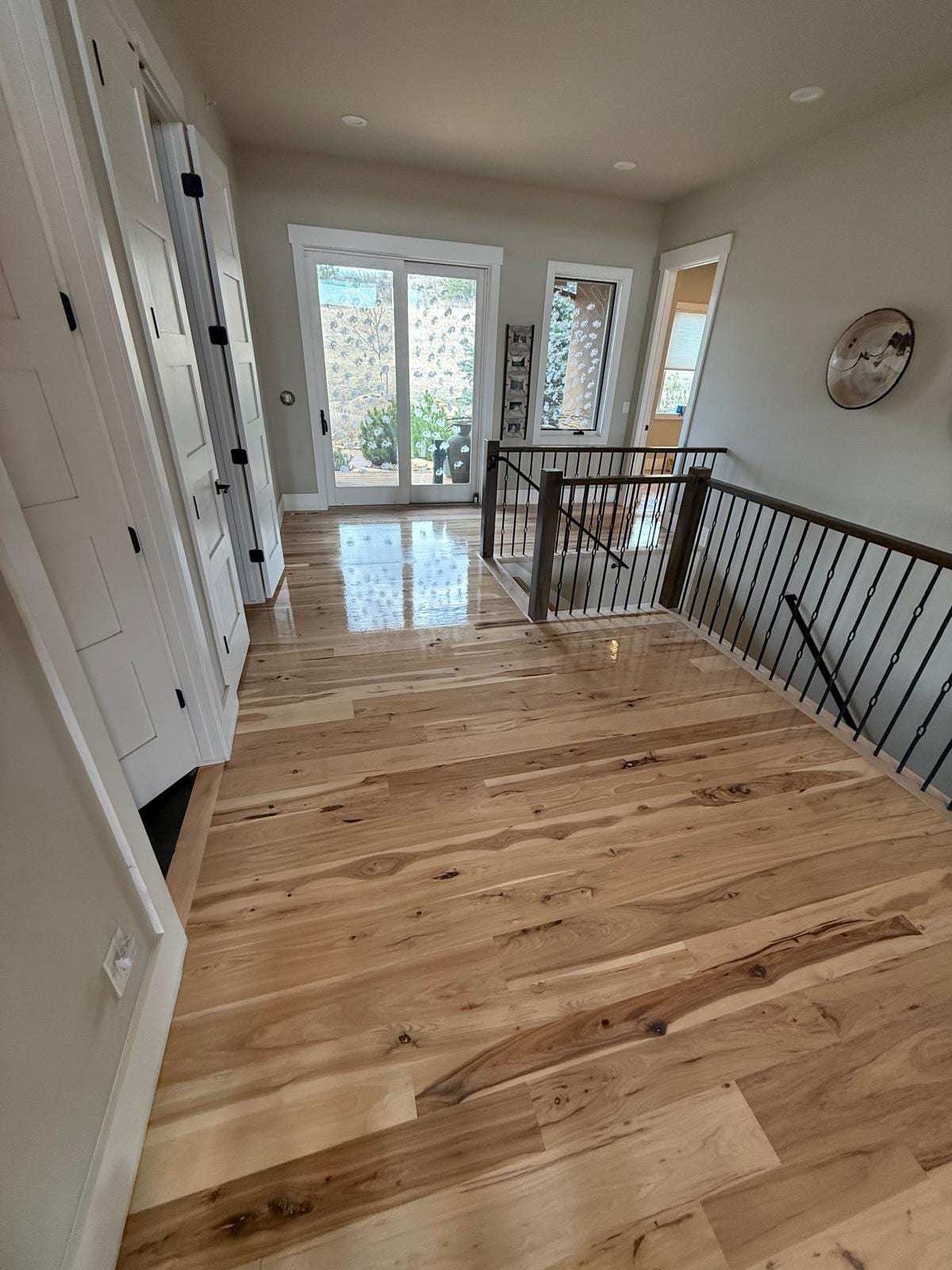 Second-floor landing and hallway with refinished hardwood flooring, black metal railing and glass doors