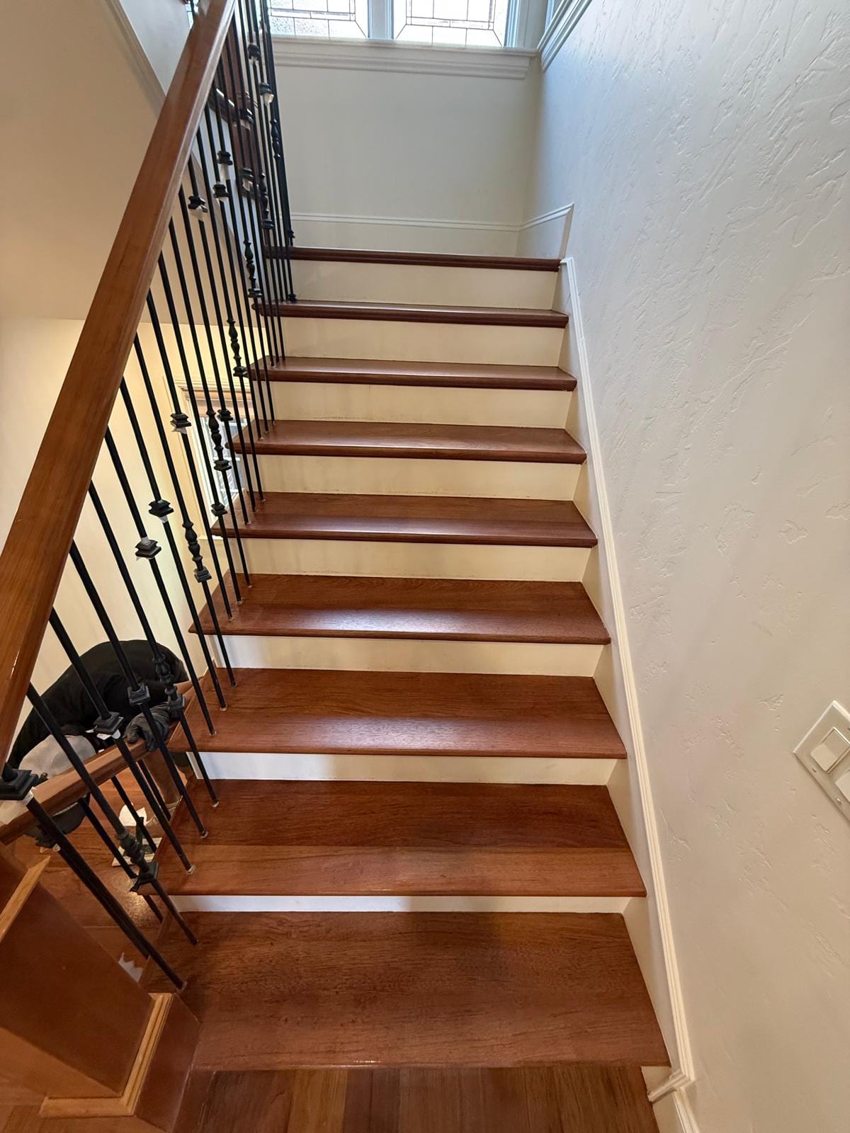 Staircase with refinished hardwood in a matching dark cherry tone, with wooden rail and black iron balusters
