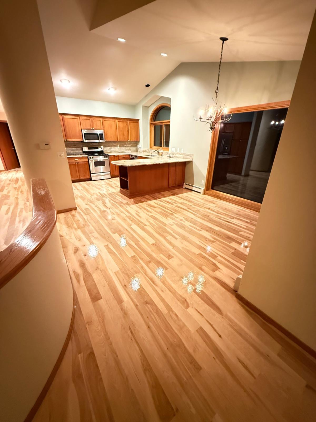 Open-plan kitchen and living space with refinished hardwood floors in a light to medium tone