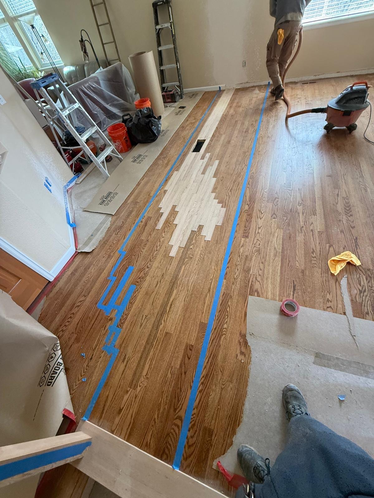 Hardwood floor installation in progress with protective tape and equipment