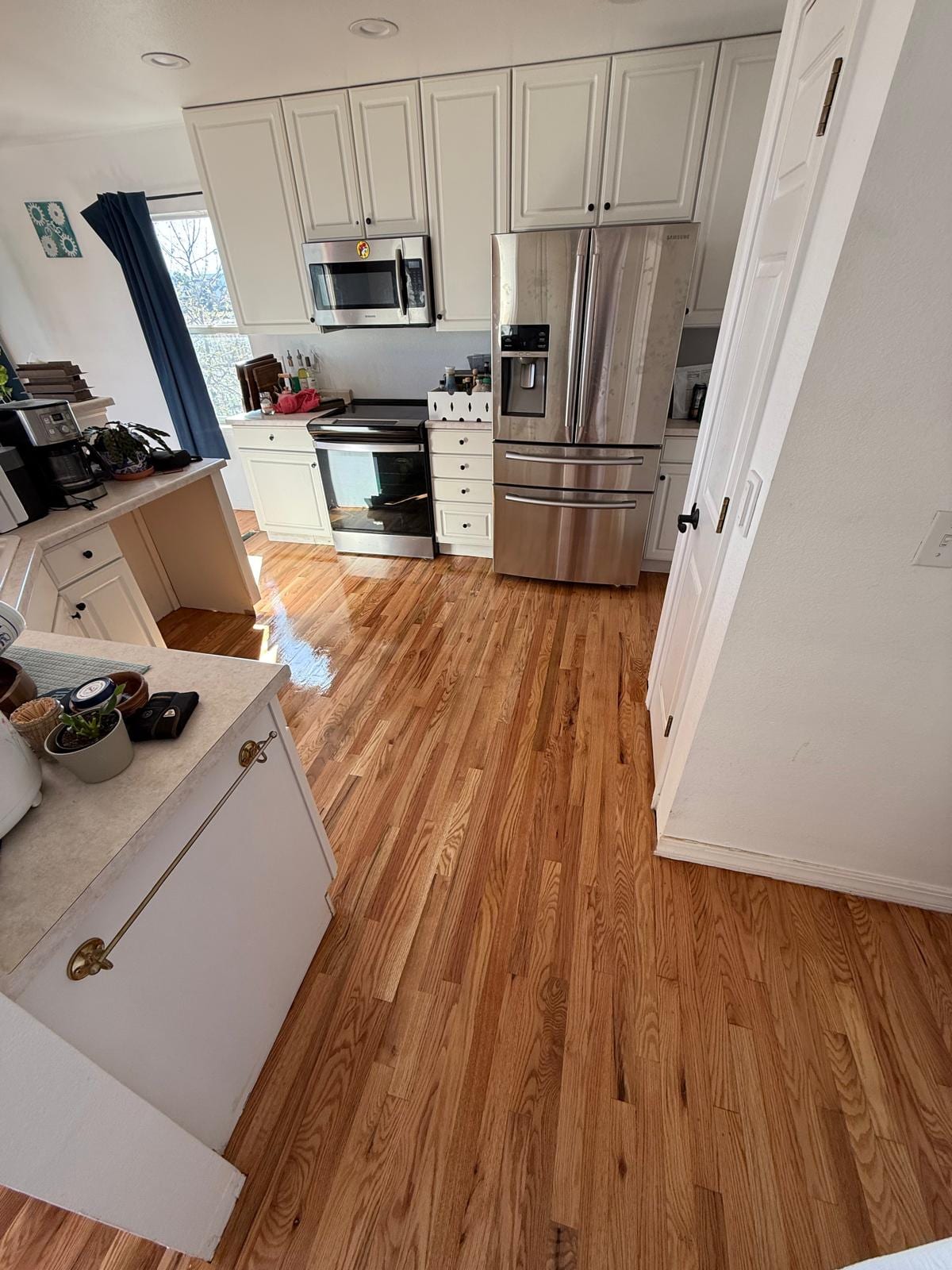 Modern kitchen with hardwood flooring in a warm medium tone, white cabinetry and stainless steel appliances