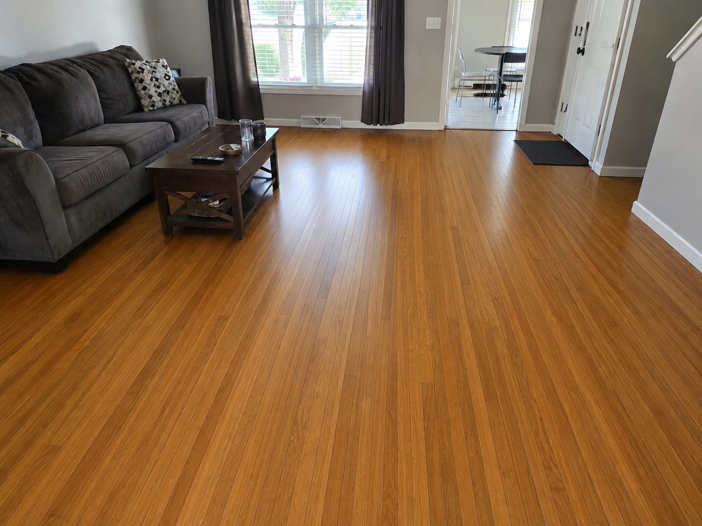 The same living room floor after sanding and refinishing, with a smooth, even, warm honey-toned finish