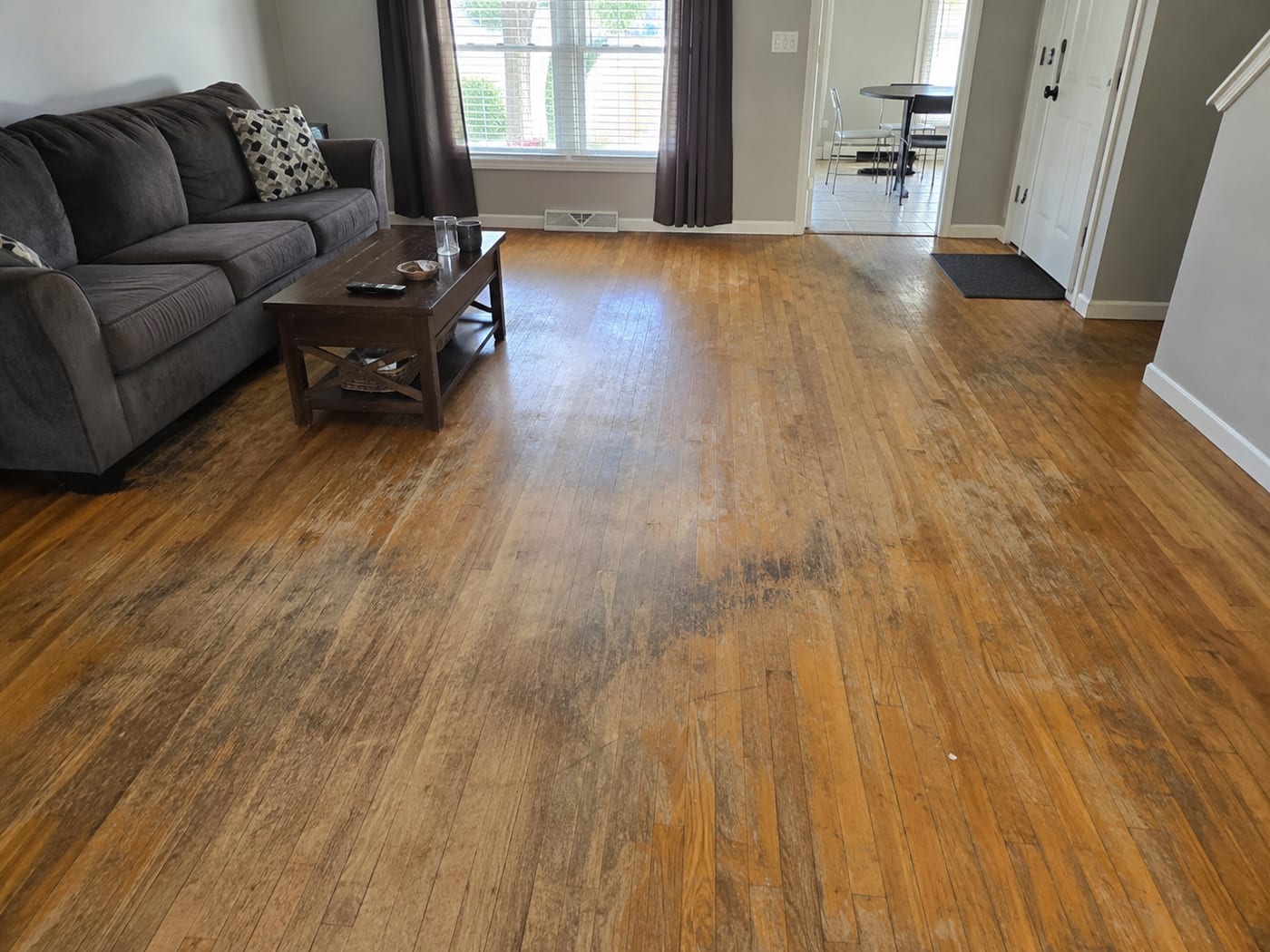 Worn, stained hardwood living room floor before refinishing
